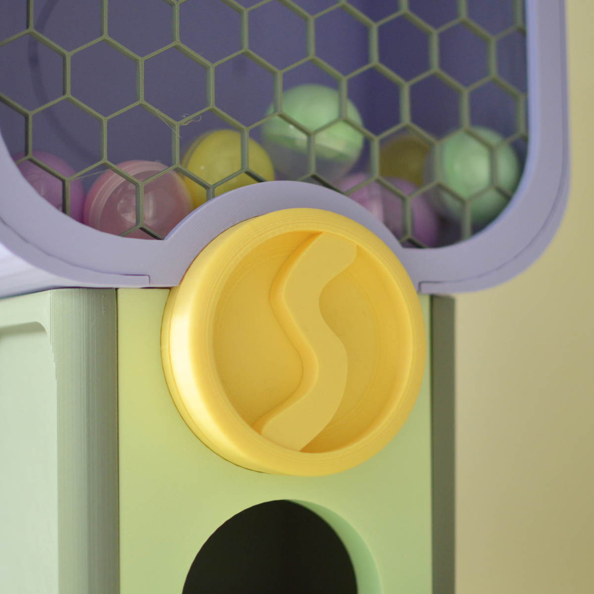 Close-up of the yellow turning knob and honeycomb capsule window of the 3D printed vending machine